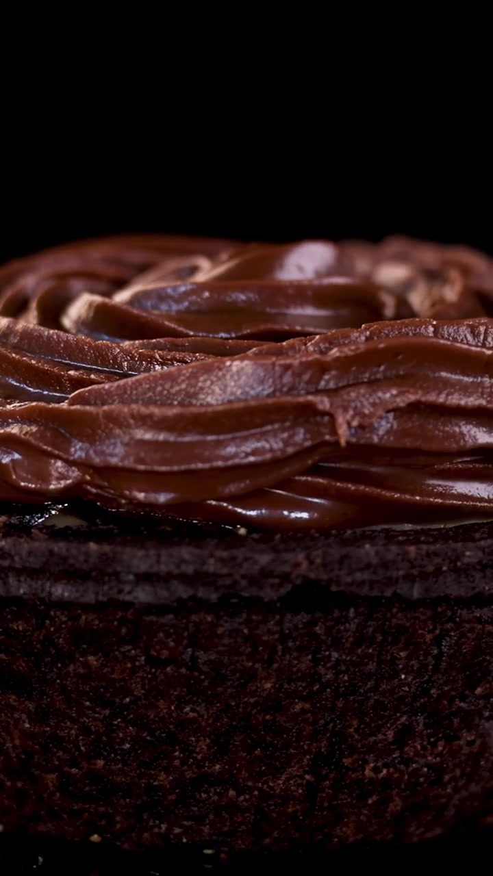 Chocolate tart with swirled frosting rotates in dramatic close-up against a dark, softly lit background.