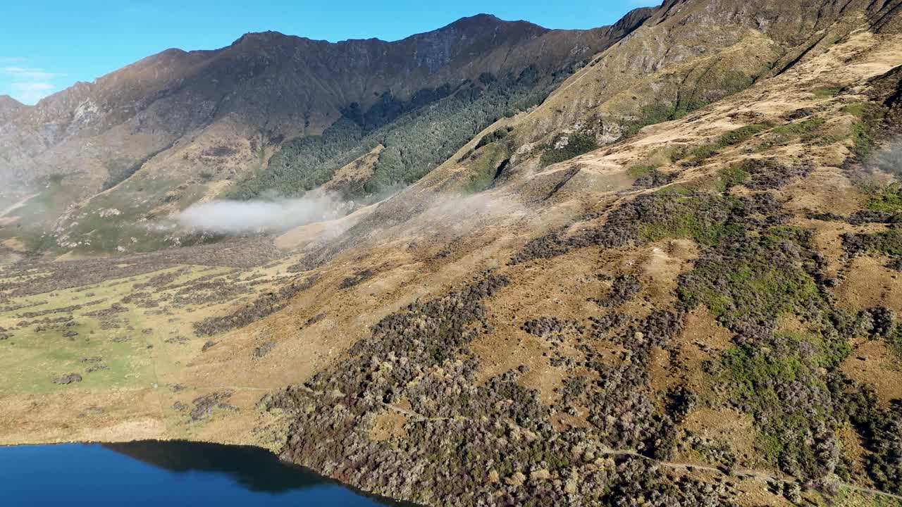 Drone footage captures the serene landscape of Lake Moke, Queenstown, with rolling hills and clear skies in natural light