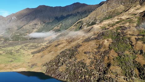 drone footage captures the serene landscape of lake moke, queenstown, with rolling hills and clear skies in natural light