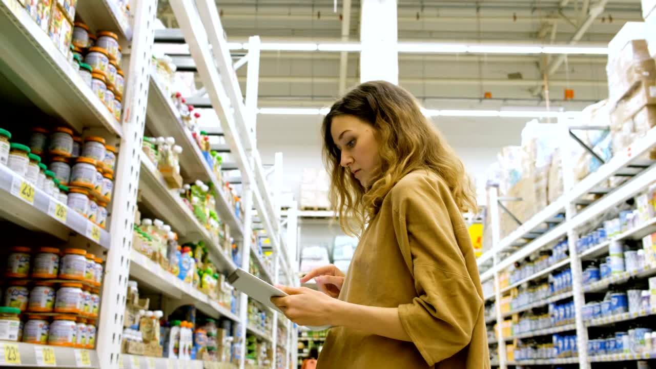 una mujer joven con una tableta recoge comida en un supermercado