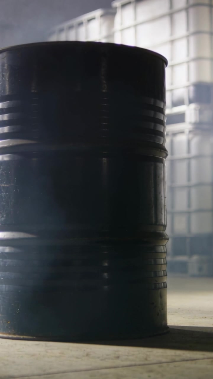 Vidéo verticale : Caméra panoramique resserrant le cadre dans un entrepôt, révélant un fût sombre et des conteneurs IBC.