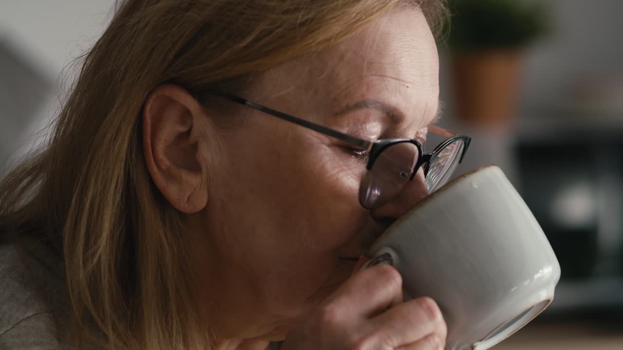 primer plano extremo de una mujer mayor caucásica pensativa sentada en un sillón, bebiendo café y mirando hacia otro lado