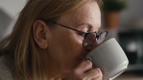 Un-Primerísimo-Plano-De-Una-Anciana-Caucásica-Pensativa-Sentada-En-Un-Sillón,-Bebiendo-Café-Y-Mirando-Hacia-Otro-Lado