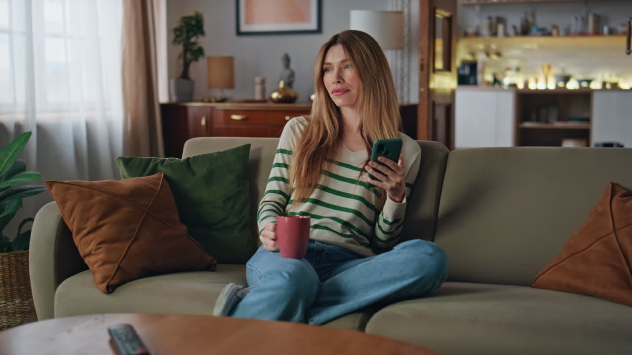 Girl relaxing coffee cup holding smartphone. Woman enjoy beverage sitting home