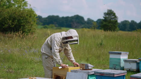 bee farmer having his beehives in the field. man checks his honey insects uniformed and protected with hat.