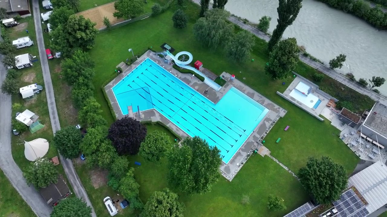 Droneoptagelse ovenfra af udendørs pool, sportsbane og flod i Schweiz.