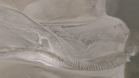 a winding water channel glistens in the sun, snaking through soft, pale sands with intricate ripples and tide-carved impressions