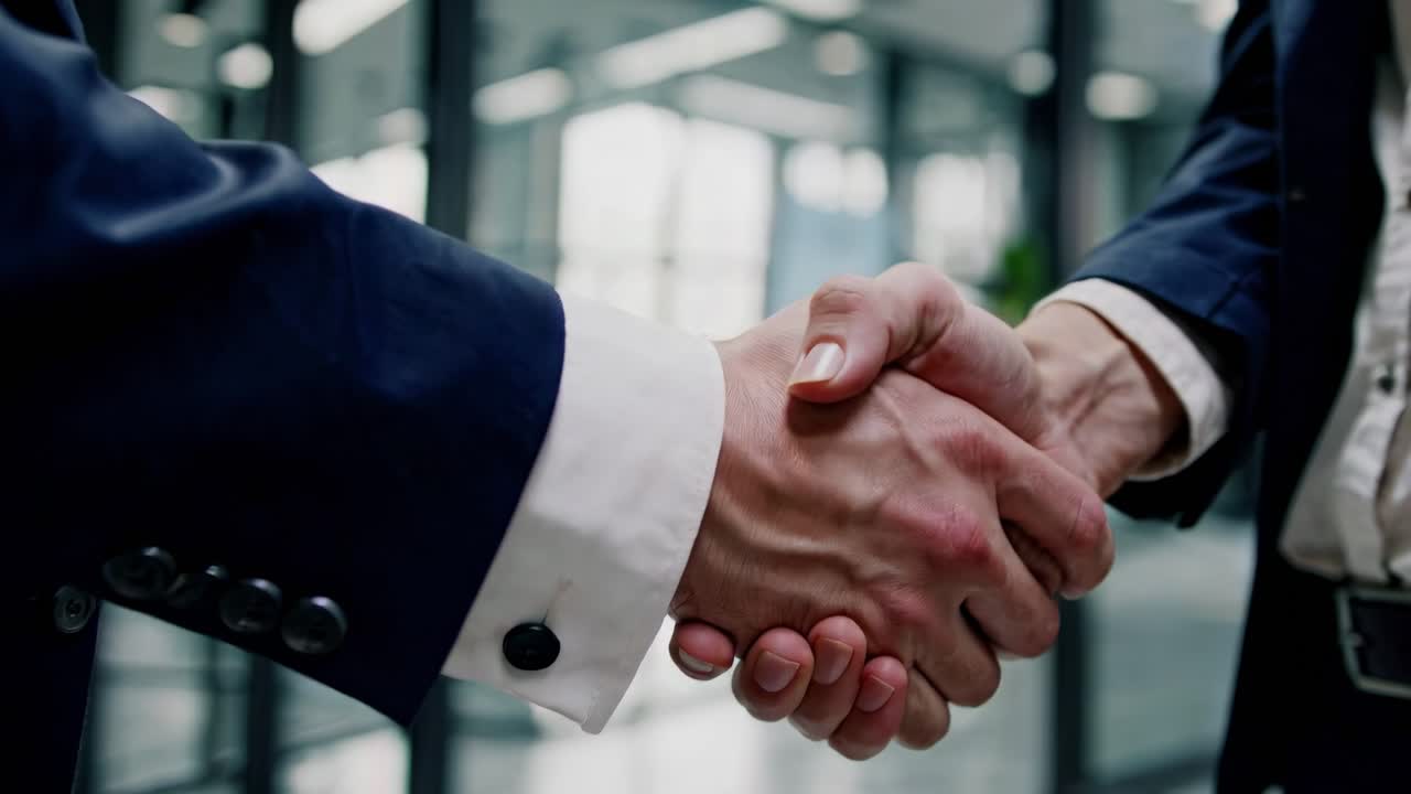 Two businessmen shaking hands in an office, finalizing a deal, with a blurred background highlighting a screen filled with graphs and charts, symbolizing success and partnership