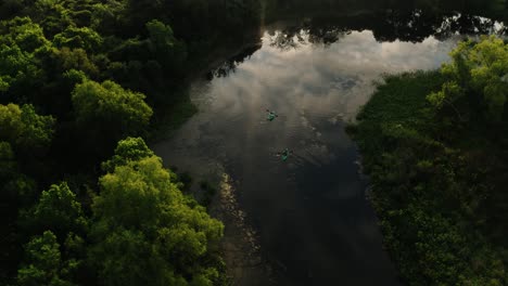 aerial drone pull away of two kayaking fisherman paddling down empty reflective waterway at sunrise