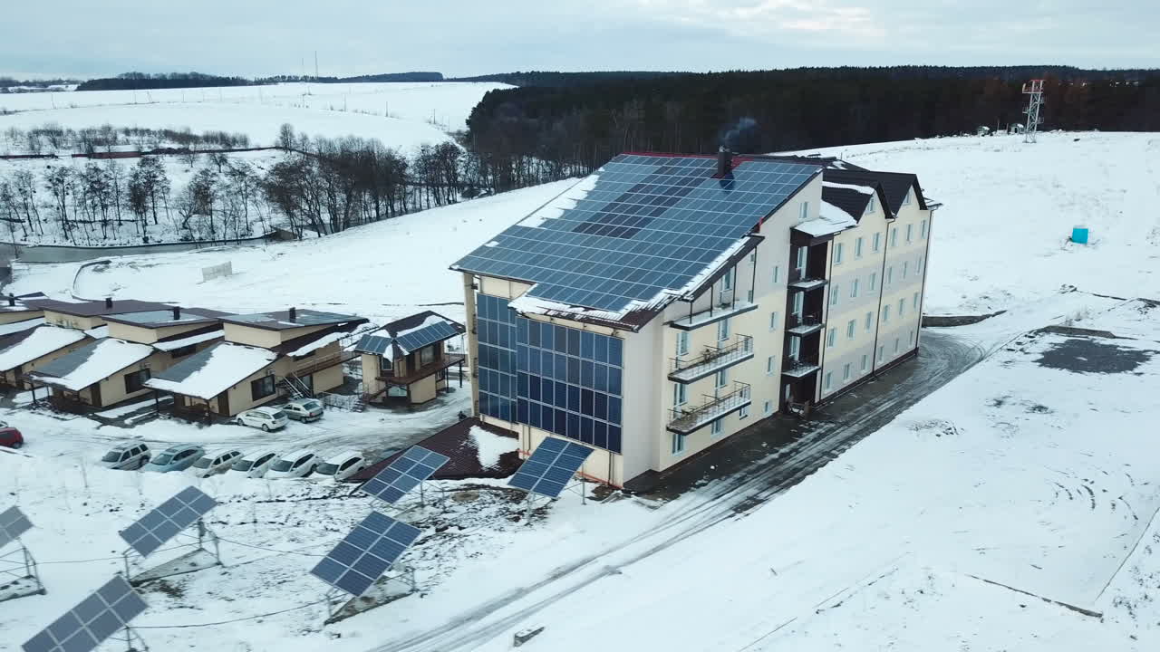 Hotel complex in the mountains with solar panels on the snow. Rows of snow covered solar panels in a small solar power plant.