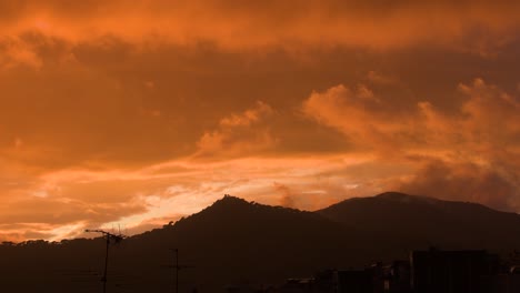 Vista-De-Montañas-Distantes-En-Una-Puesta-De-Sol-Naranja-Mientras-En-El-Cielo-Las-Nubes-Se-Mueven-Lentamente