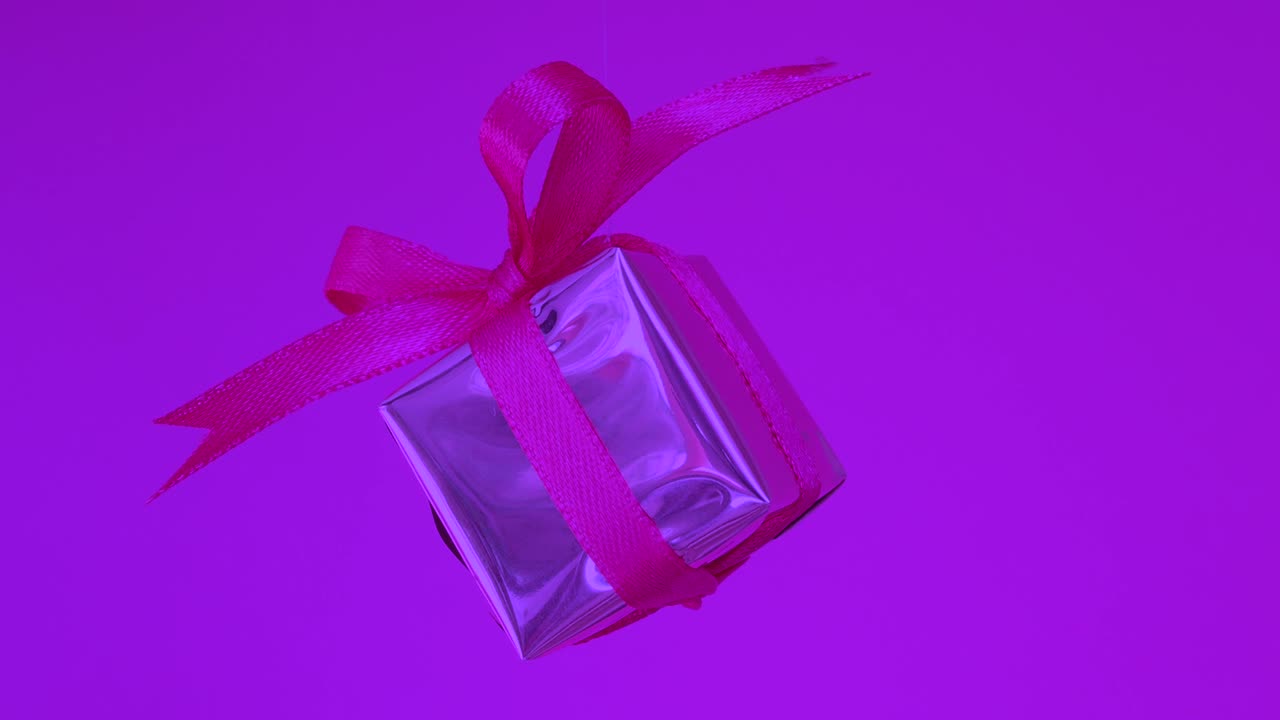 caja de regalos con cinta roja girando sobre un fondo púrpura de neón. rotación de 360 grados