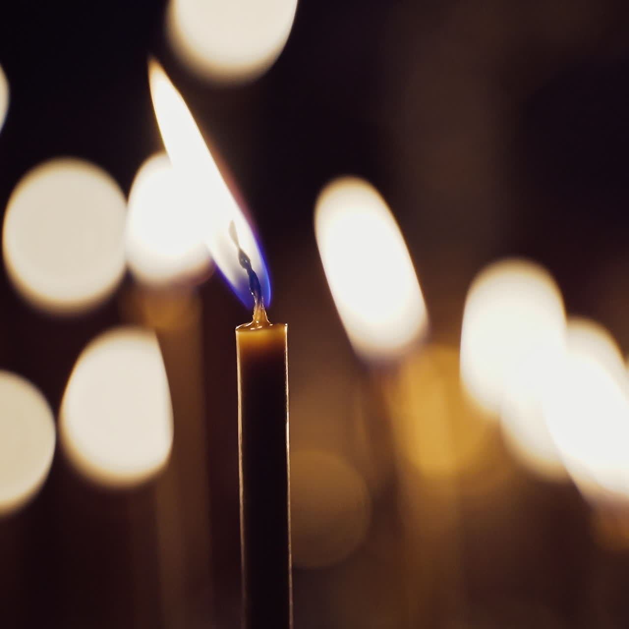 Una candela che brucia luminosamente sulle luci sfocate. Le candele sono accese per intenzioni di preghiera nel tempio notturno. Primo piano