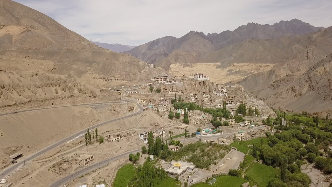camino sinuoso en la tierra de la luna con exuberantes álamos verdes en primer plano cerca del monasterio y el pueblo de lamayuru en leh, ladakh, india