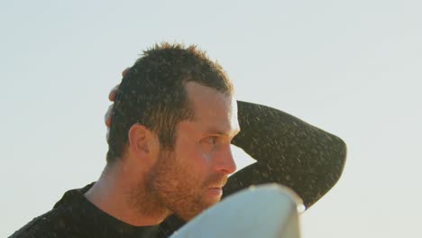 Side-view-of-mid-adult-caucasian-male-surfer-with-surfboard-standing-at-beach-during-sunset-4k