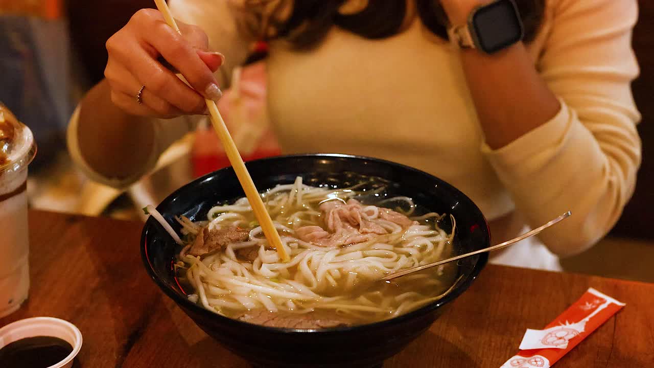 A person enjoys a bowl of Vietnamese pho in a cozy restaurant setting with warm lighting