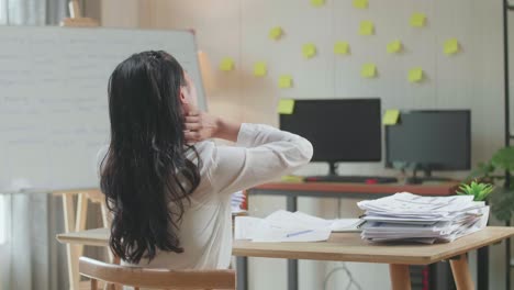 vista trasera de una mujer asiática estirándose después de trabajar duro con documentos en la oficina