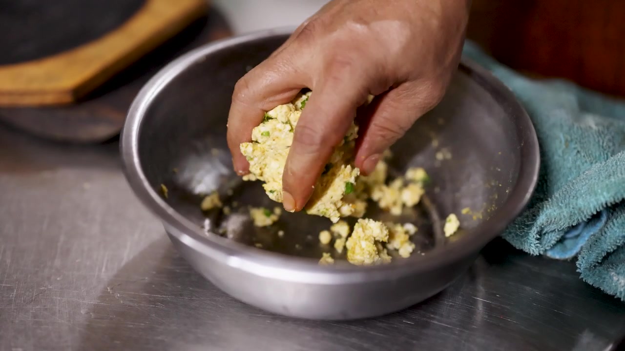 Primo piano di uno chef che impasta a mano il paneer condito in una ciotola di metallo