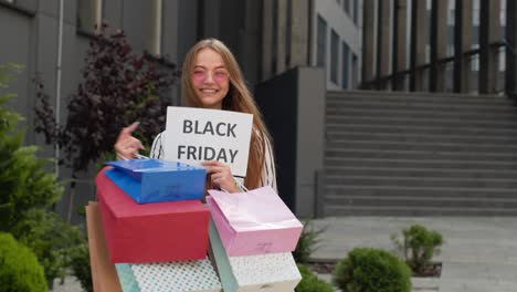 joyful teen girl showing black friday inscription, smiling, looking satisfied with low prices