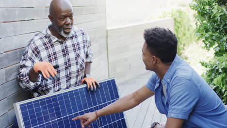 padre afroamericano mostrando el panel solar al hijo adulto en el jardín soleado, cámara lenta