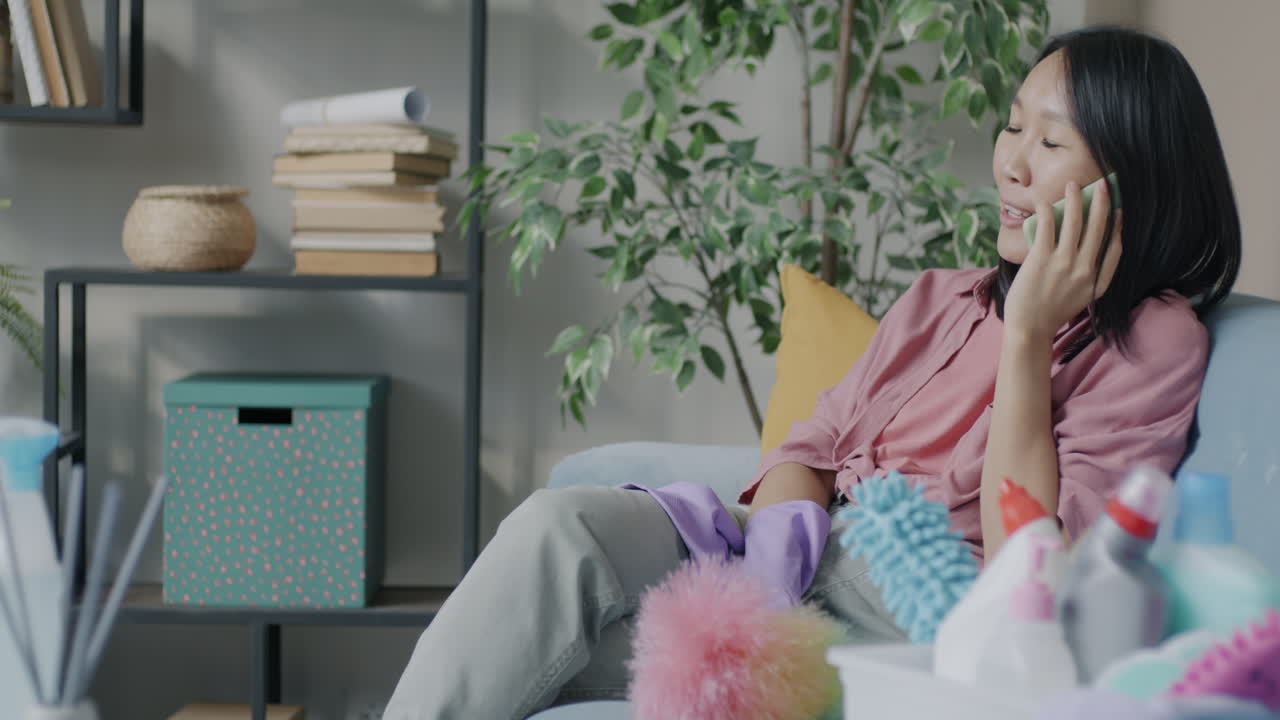Woman on Couch Talking on Phone While Cleaning
