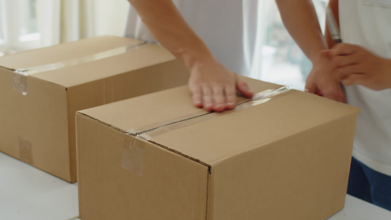 Hands of Volunteers Packing Donation Boxes with Tape