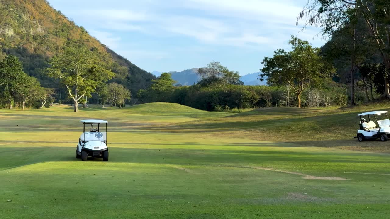 A golf cart travels along a lush, green fairway surrounded by trees and hills.