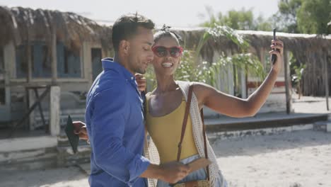 Happy-diverse-couple-arriving-at-beach-hotel,-taking-selfie-and-man-carrying-woman,-in-slow-motion