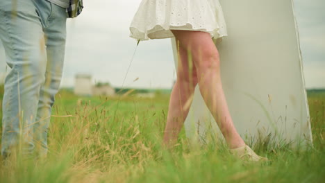a front shot of a couple's legs walking through a grassy field. the man wears jeans and black shoes, while the woman, dressed in a short gown, walks beside him. natural, relaxed movement of the couple
