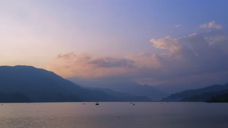 Un-Lapso-De-Tiempo-De-Barcos-En-Un-Lago-Al-Atardecer-Con-Montañas-Al-Fondo