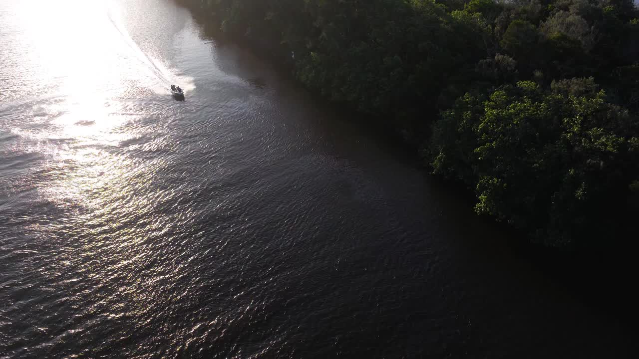 Aerial view of a speedboat navigating a river, surrounded by lush greenery, under bright sunlight