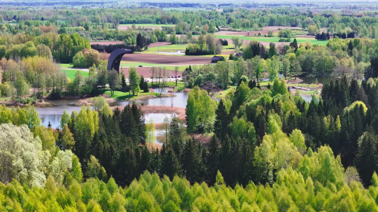 Biržai Regional Park, Lithuania - A Scenic View of the Karst Lake Framed by Dense Foliage, With the Kirkilai Observation Tower Rising in the Background - Aerial Drone Shot