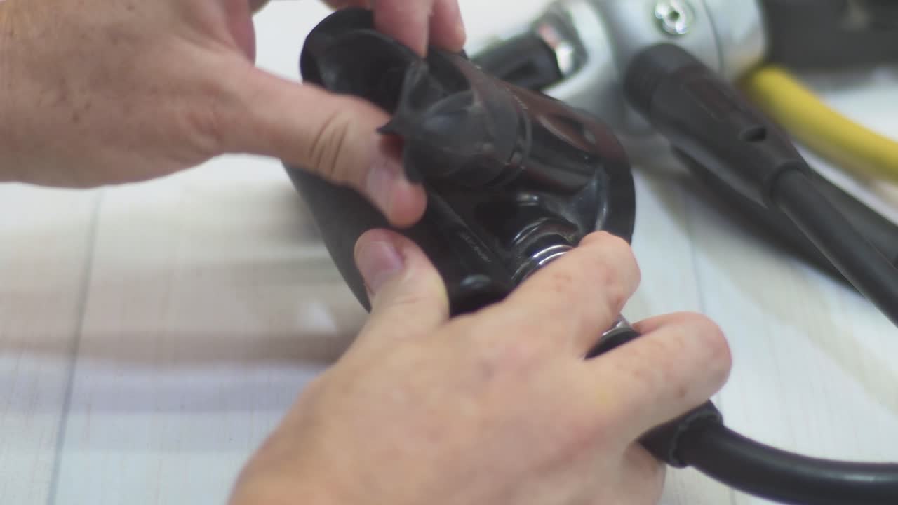Close-up of a woman’s hands checking a scuba diving regulator, inspecting the mouthpiece and hoses, breathing through the second stage to ensure no air leaks