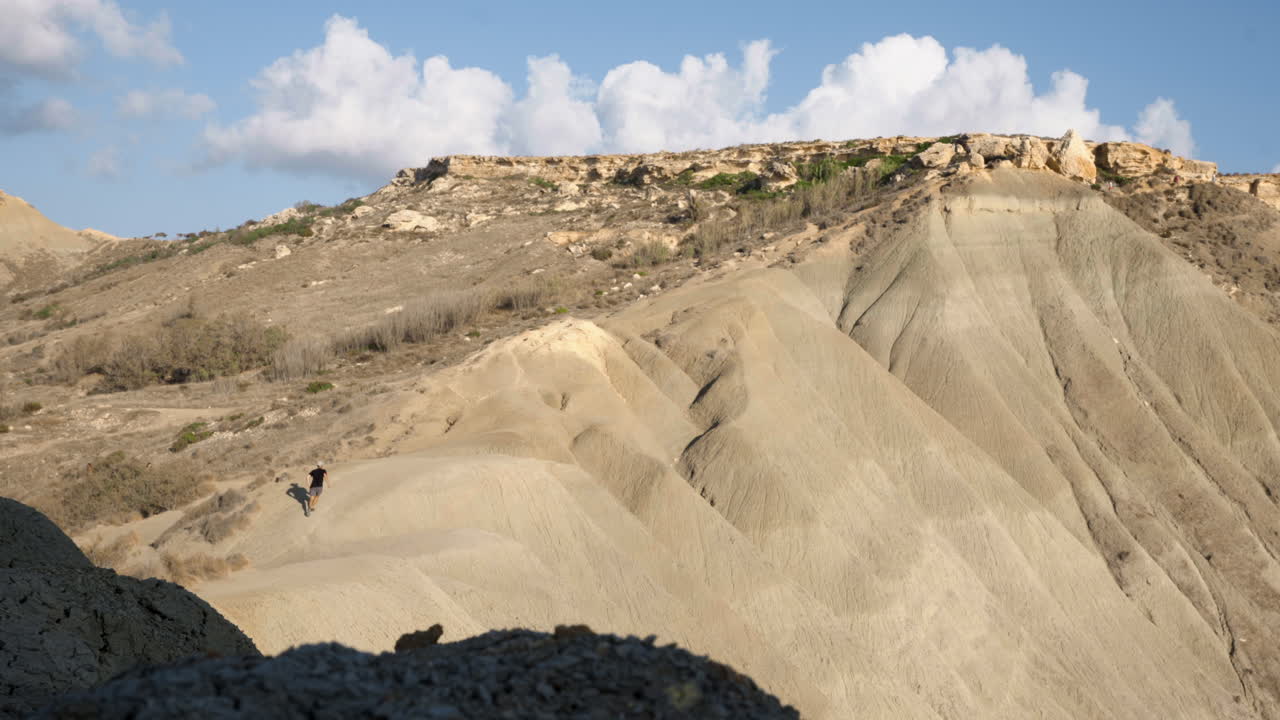 hombre caucásico caminando por acantilados de dunas en malta en un día soleado