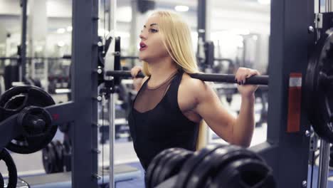 Starke-Junge-Blonde-Frau-Mit-Schönem,-Athletischem-Körper-Im-Schwarzen-Outfit-Beim-Kniebeugentraining-Mit-Der-Langhantel-Im-Fitnessstudio