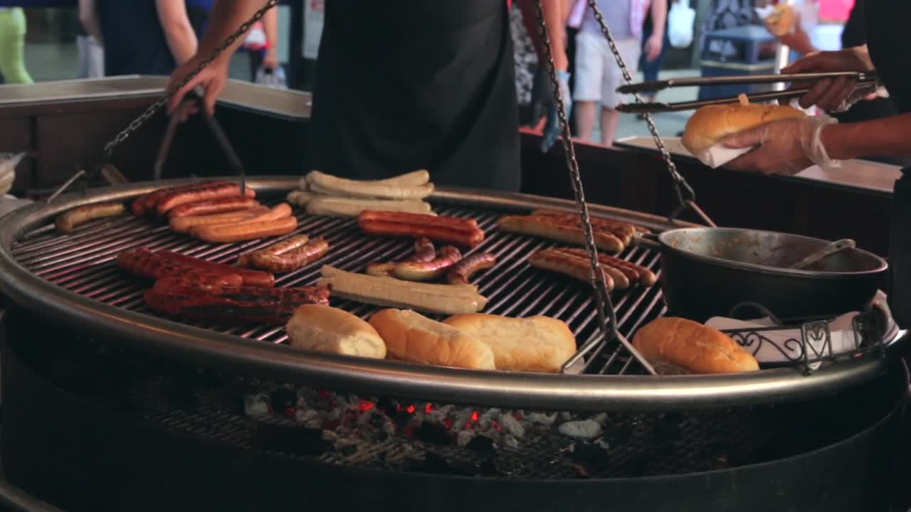 German sausages cooking on an open fire pit barbecue at a street food market.