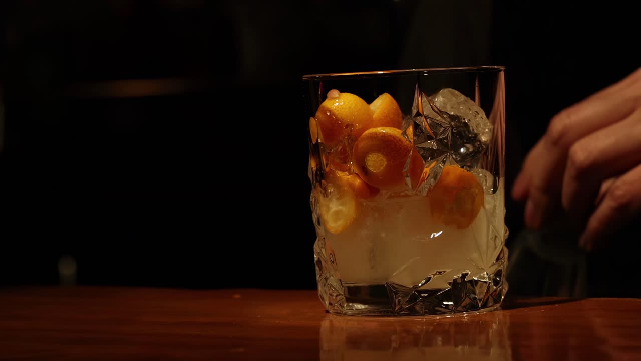 A close-up view of a citrus drink being poured into a glass with ice and citrus slices.