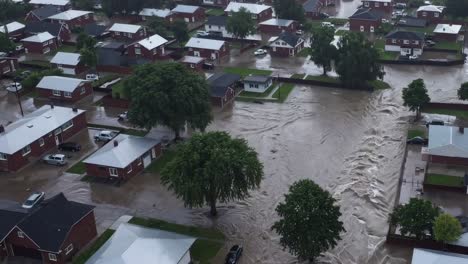 raging floodwaters surging through residential neighborhood, completely submerging houses and streets during catastrophic natural disaster causing widespread destruction and water damage