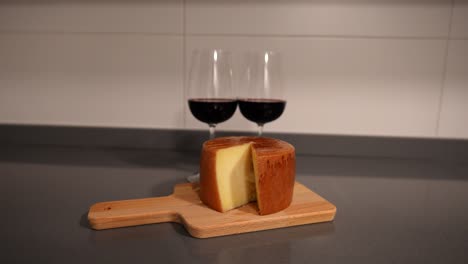 zoom out toma de un gran rollo de queso cortado en la tabla de corte y dos vasos de vino tinto