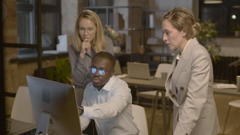 american businessman showing something on computer to his two female colleagues and discussing together in the office 1