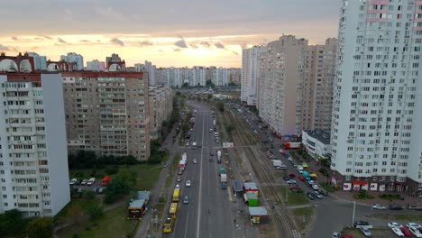 Vista-Aérea-Con-Vista-A-Los-Autos-En-Una-Avenida,-Entre-Un-Antiguo-Edificio-De-Apartamentos,-Durante-La-Puesta-De-Sol,-En-El-Barrio-Troieshchyna-De-Kiev,-Ucrania---Reversa,-Tiro-Con-Drones