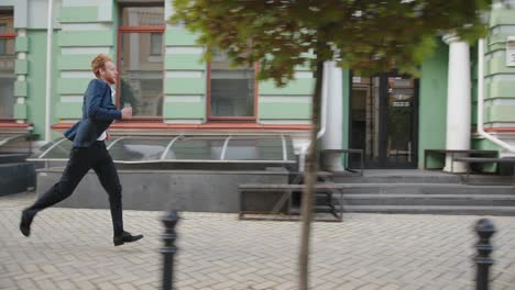 young man in office suit with smartphone runs along street