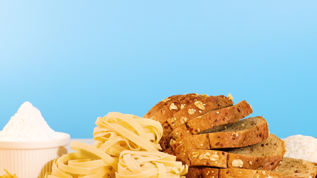A variety of grains, pasta, and bread arranged on a table with a bright blue backdrop, showcasing diverse textures and colors