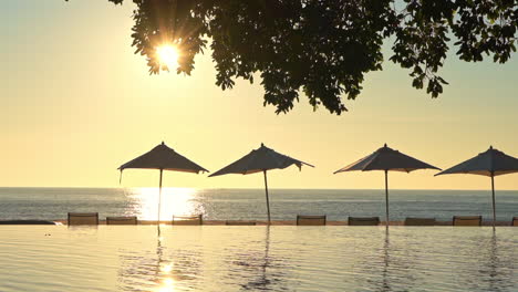 Amazing-view-of-the-sunset-at-the-infinity-pool-area,-line-of-Beach-Umbrellas-and-deck-chairs-in-the-foreground