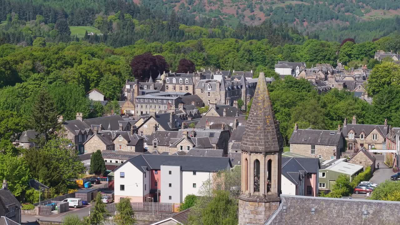 Panoramic drone orbit of Pitlochry, Scotland, featuring the church bell tower and the charming village surrounded by green hills and scenic landscapes