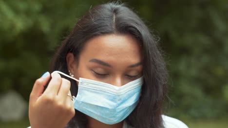 portrait of a beautiful dark haired young woman taking off protective medical face mask then smile