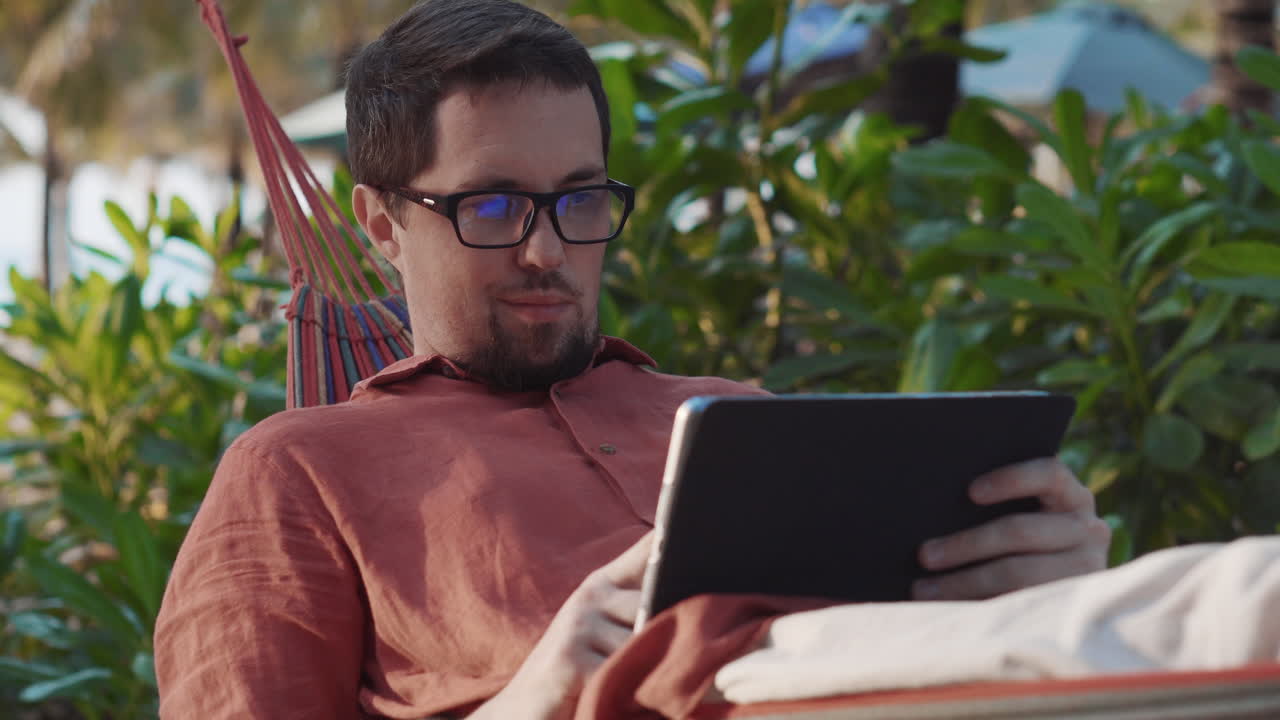 hombre relajándose en una hamaca con una tableta
