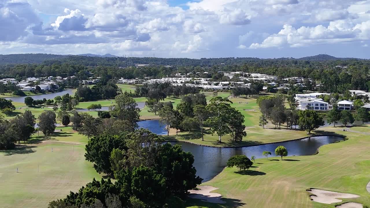 Cropped aerial footage showcasing a golf course with a pond, surrounded by trees and residential buildings.
