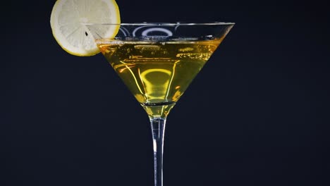 a close-up of a yellow cocktail in a martini glass, garnished with a lime slice against a dark backdrop.