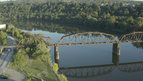 high orbiting drone shot of a rail road truss bridge crossing a river at sunrise